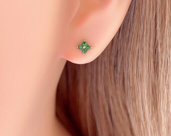 Könnte beinhalten: Nahaufnahme eines Ohrs mit einem kleinen silbernen Ohrstecker. Der Ohrring hat ein vierblättriges Kleeblatt-Design mit kleinen, leuchtend grünen Edelsteinen. Der Ohrring ist vor der Haut des Ohrs platziert.