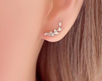 May include: Silver earrings with a delicate, curved design featuring small, clear cubic zirconia stones. The earrings are a minimalist and elegant style.