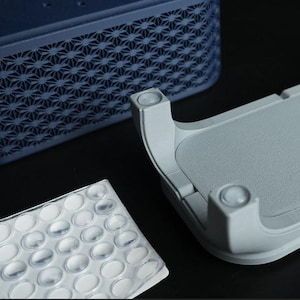 May include: An abstract image of three components. A dark blue, rectangular object with a geometric pattern, a light gray, curved object with rounded edges, and a clear, plastic sheet with oval-shaped bumps.