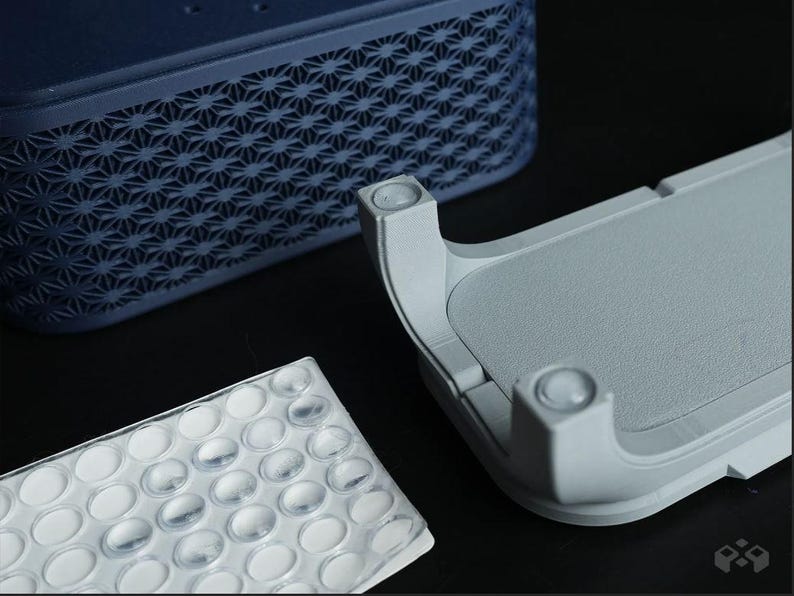 May include: An abstract image of three components. A dark blue, rectangular object with a geometric pattern, a light gray, curved object with rounded edges, and a clear, plastic sheet with oval-shaped bumps.