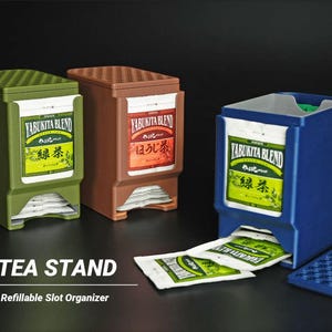 以下が含まれることがあります： 緑、茶色、青の3つのティースタンド。各スタンドにはディスペンサーのスロットがあります。「YABUKITA BLEND」のブランドと日本語のテキストが表示されています。ティーバッグがディスペンサースロットに見えます。「TEA STAND」と「Refillable Slot Organizer」の文字が下にあります。