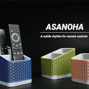Può includere: Organizzatori per telecomandi blu, verdi e arancioni, ciascuno con un motivo geometrico. L'organizzatore blu contiene due telecomandi. Il testo "ASANOHA" e "A subtle rhythm for remote controls" sono visualizzati.