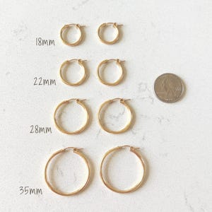 May include: Gold-colored hoop earrings in four sizes: 18mm, 22mm, 28mm, and 35mm. The earrings are displayed in pairs, with a US quarter for size comparison. The earrings are on a white surface.