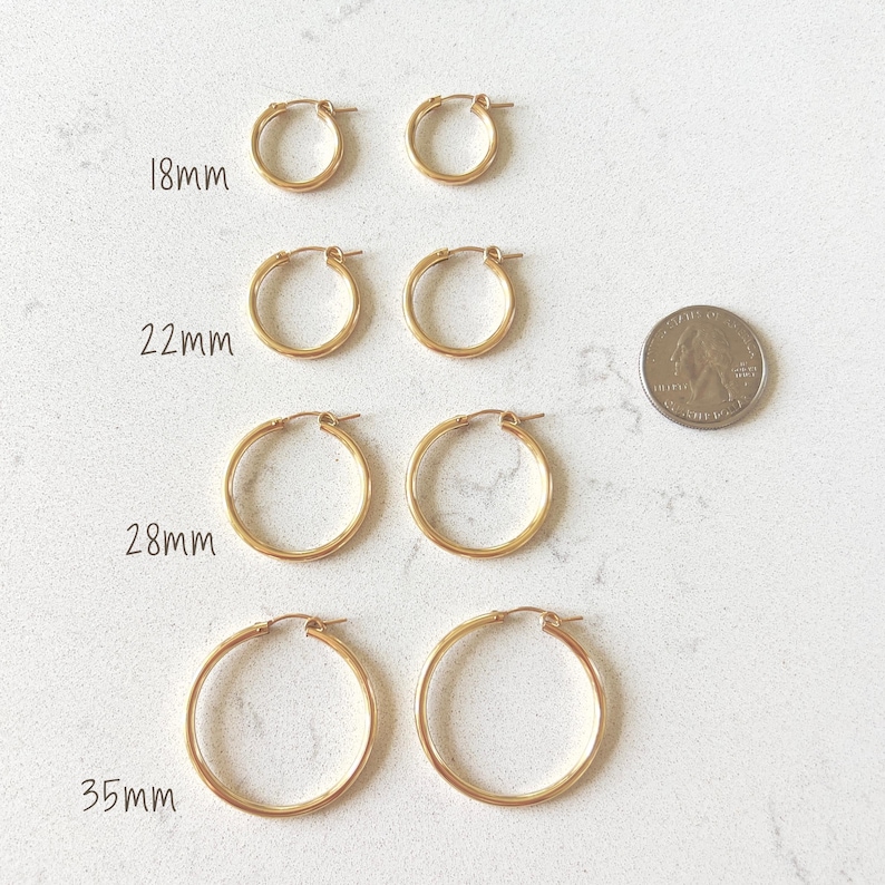 May include: Gold-colored hoop earrings in four sizes: 18mm, 22mm, 28mm, and 35mm. The earrings are displayed in pairs, with a US quarter for size comparison. The earrings are on a white surface.