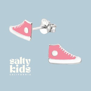 May include: A pair of silver stud earrings featuring a pink sneaker design. The earrings are a fun and trendy accessory for kids.