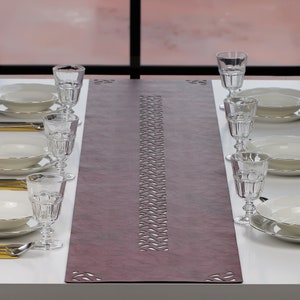 Peut inclure: Un chemin de table violet avec un motif découpé décoratif. Le chemin de table est placé sur une table blanche avec des assiettes et des verres.
