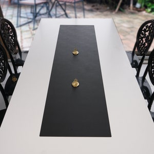 Può includere: Un runner da tavolo nero su uno sfondo bianco. Due oggetti decorativi dorati sono posizionati sul runner.