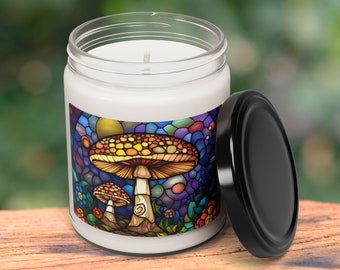 May include: A white candle jar with a black lid. The jar has a colorful stained glass design of mushrooms on the front. The design features a large mushroom with a red and yellow cap and a smaller mushroom with a brown cap.
