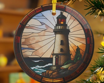 May include: Round glass ornament with a stained glass design of a lighthouse on a rocky shore with waves crashing against the rocks. The lighthouse is white with a red roof and a black door. The sky is blue with white clouds. The ornament has a yellow ribbon attached to it.