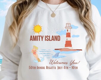 May include: White sweatshirt with a graphic design of a lighthouse, a sun, a shark fin, and a person waterskiing. The text "Amity Island" and "Welcomes You!" is printed on the sweatshirt. The text "50th Annual Regatta July 4th - 10th" is also printed on the sweatshirt.