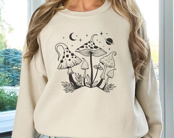 May include: A beige sweatshirt with a black and white graphic of mushrooms and stars. The graphic includes a crescent moon and a planet.