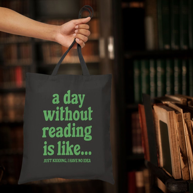 Op de afbeelding: Zwarte tote bag met groene tekst die "a day without reading is like... JUST KIDDING. I HAVE NO IDEA" zegt.