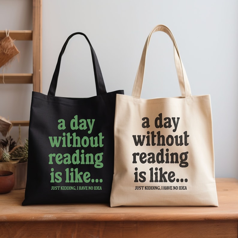 Op de afbeelding: Twee tote bags met de tekst "a day without reading is like... JUST KIDDING, I HAVE NO IDEA" erop gedrukt. E&eacute;n tas is zwart met groene tekst en de andere is beige met zwarte tekst.