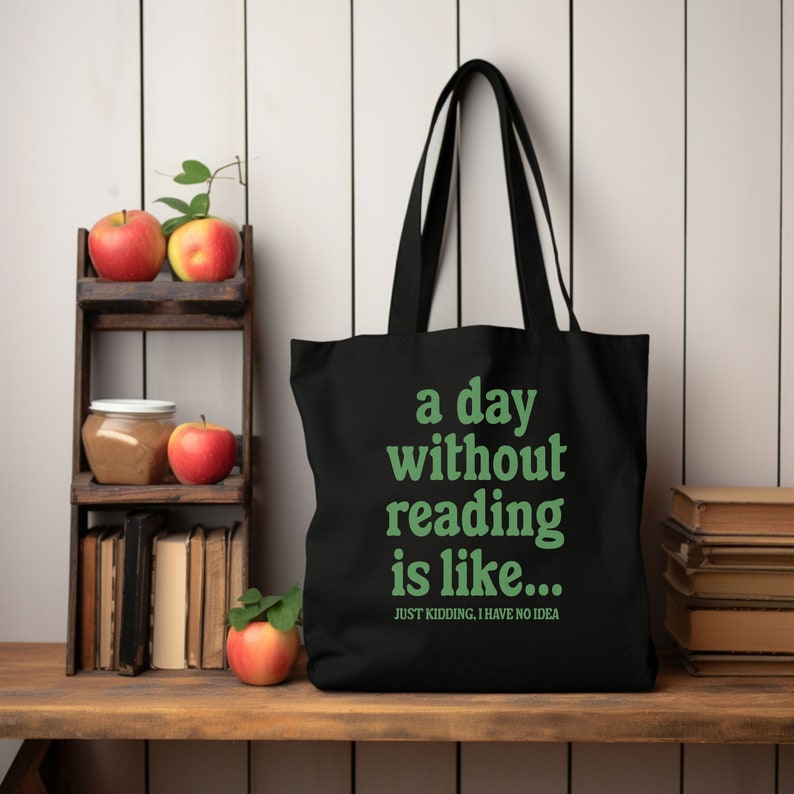 Op de afbeelding: Zwarte tote bag met witte tekst die "a day without reading is like... JUST KIDDING, I HAVE NO IDEA" zegt. De tekst is groen.