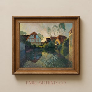 Classic village scene artwork displayed in an ornate gold-toned frame with decorative molding, mounted on a cream-colored wall.