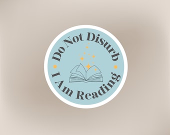 May include: A blue and white round sticker with the text "Do Not Disturb I Am Reading" and a black and white illustration of an open book with yellow stars above it.