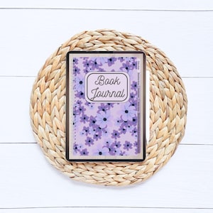 May include: A purple and white floral patterned book journal with the text "Book Journal" in a brown rectangle on the cover.