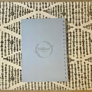 May include: A light gray spiral bound notebook with a silver logo that says "Wildflower Craft Co. Est. 2022" on the front cover.