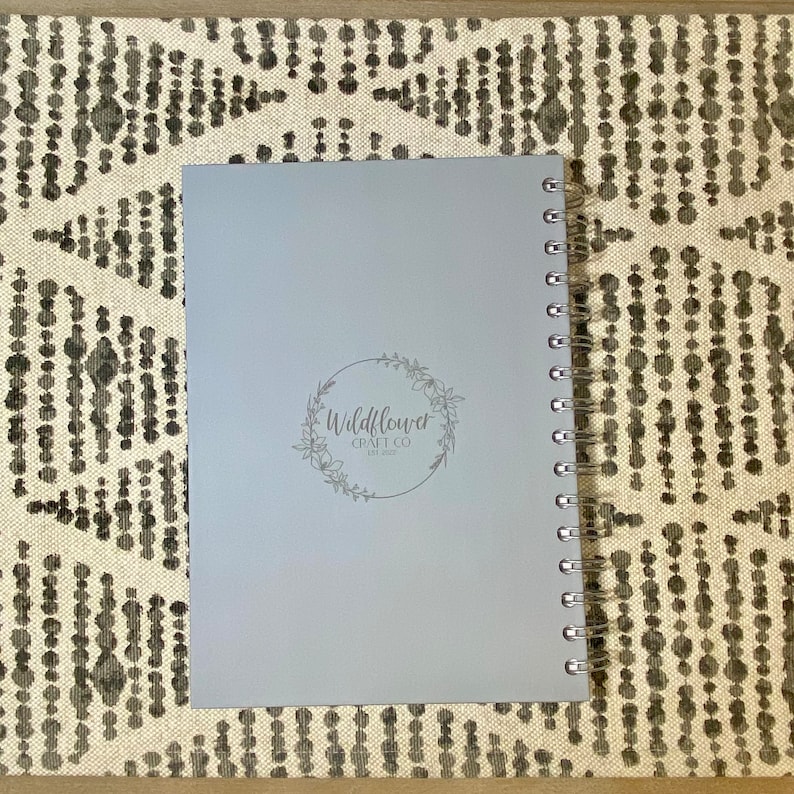 May include: A light gray spiral bound notebook with a silver logo that says "Wildflower Craft Co. Est. 2022" on the front cover.