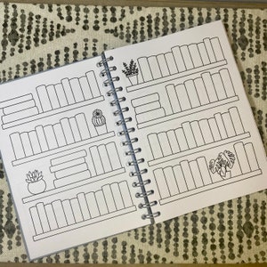 May include: A black and white book with a spiral binding. The pages are filled with outlines of bookshelves with spaces to fill in the titles of books. There are also outlines of plants on the shelves.