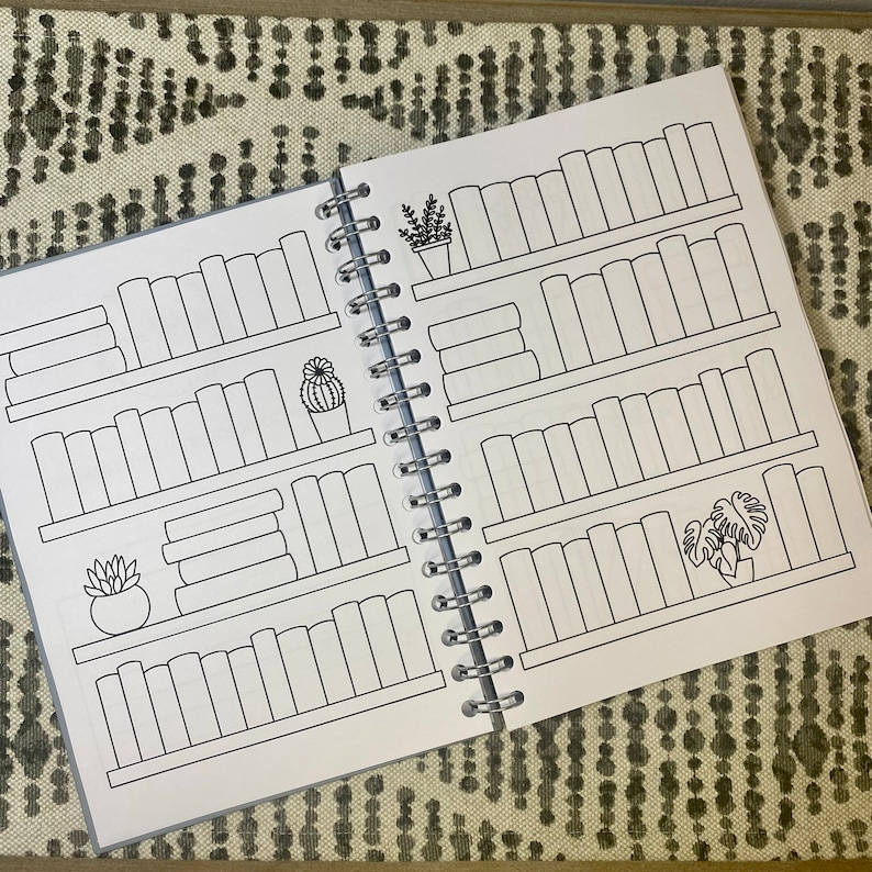 May include: A black and white book with a spiral binding. The pages are filled with outlines of bookshelves with spaces to fill in the titles of books. There are also outlines of plants on the shelves.