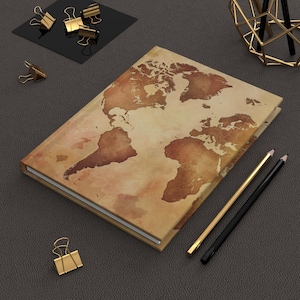 Op de afbeelding: Een bruin lederen gebonden dagboek met een vintage wereldkaartontwerp op de omslag. Het dagboek ligt op een bruin oppervlak met twee potloden en een paar gouden paperclips.