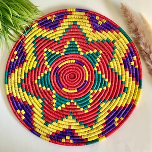 Pode incluir: Uma tapeçaria de parede redonda tecida com círculos concêntricos de vermelho, amarelo, verde e roxo.