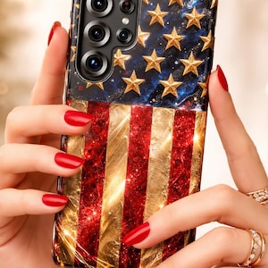 Puede incluir: Una funda rectangular para smartphone con un dise&ntilde;o inspirado en la bandera estadounidense, que presenta una secci&oacute;n superior azul oscuro adornada con estrellas doradas y una secci&oacute;n inferior con franjas verticales alternas de purpurina roja y oro.