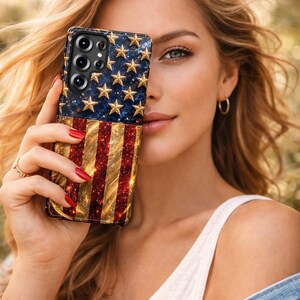 Puede incluir: Una funda rectangular para smartphone con un dise&ntilde;o brillante de la bandera estadounidense. La secci&oacute;n superior muestra estrellas doradas sobre un fondo azul oscuro, mientras que la inferior presenta rayas rojas y doradas con purpurina.