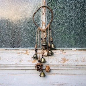 May include: A rustic-style wind chime with a wooden ring and multiple small bells hanging from it. The bells are made of metal and have a natural finish. The wind chime is decorated with small wooden beads and pinecones.