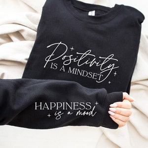 May include: Black sweatshirt with white text that reads "Positivity is a mindset" and "Happiness is a mood".