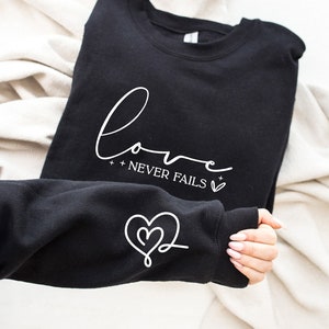 May include: Black sweatshirt with the text "love + never fails +" in white lettering and a white heart on the front. The sweatshirt has a white heart with a swirl design on the sleeve.