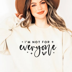 May include: A white sweatshirt with the text "I'm not for everyone" in black script lettering. The sweatshirt has a small heart symbol and stars on either side of the text.