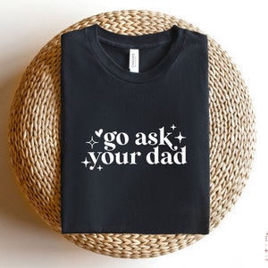 May include: Black t-shirt with white text that says "go ask your dad" with a heart and stars around the text.