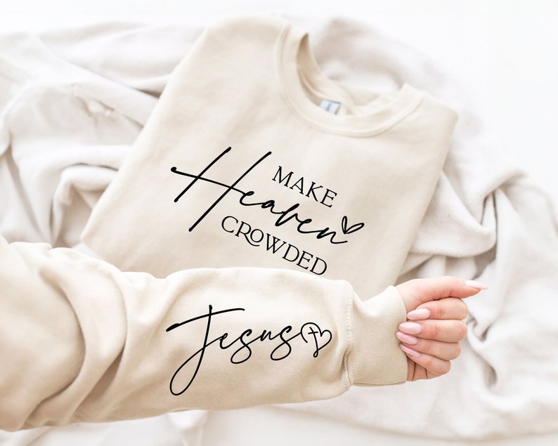 Puede incluir: Una sudadera beige con el texto "Make Heaven Crowded" y un coraz&oacute;n en la parte delantera y el texto "Jesus" y un coraz&oacute;n en la manga.