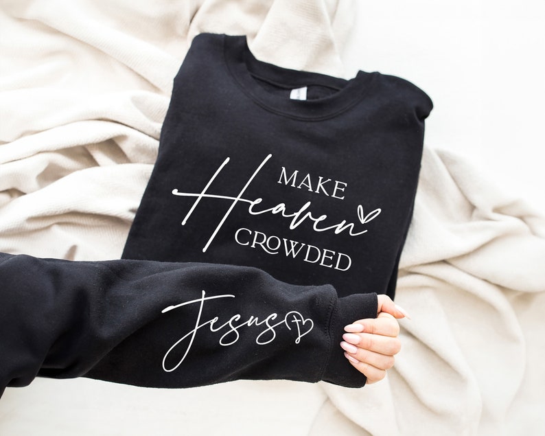 Puede incluir: Sudadera negra con texto blanco que dice "Make Heaven Crowded" y un s&iacute;mbolo de coraz&oacute;n. La manga de la sudadera tiene texto blanco que dice "Jesus" y un s&iacute;mbolo de coraz&oacute;n.