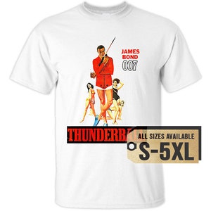May include: White t-shirt with a vintage poster of James Bond 007 from the movie "Thunderball". The poster features a man in a red shirt and white shorts holding a spear, with three women behind him. The text "JAMES BOND 007" is printed in black above the poster. The text "THUNDERBALL" is printed in red below the poster. The t-shirt is available in sizes S-5XL.