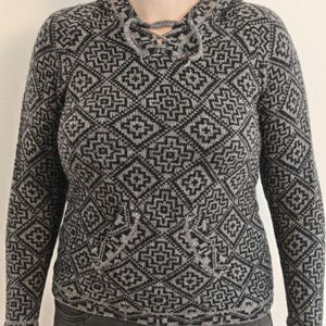 May include: A gray and black hooded sweater with a geometric pattern. The sweater features a drawstring neckline, long sleeves, and a front pocket. The pattern is a repeating diamond design.