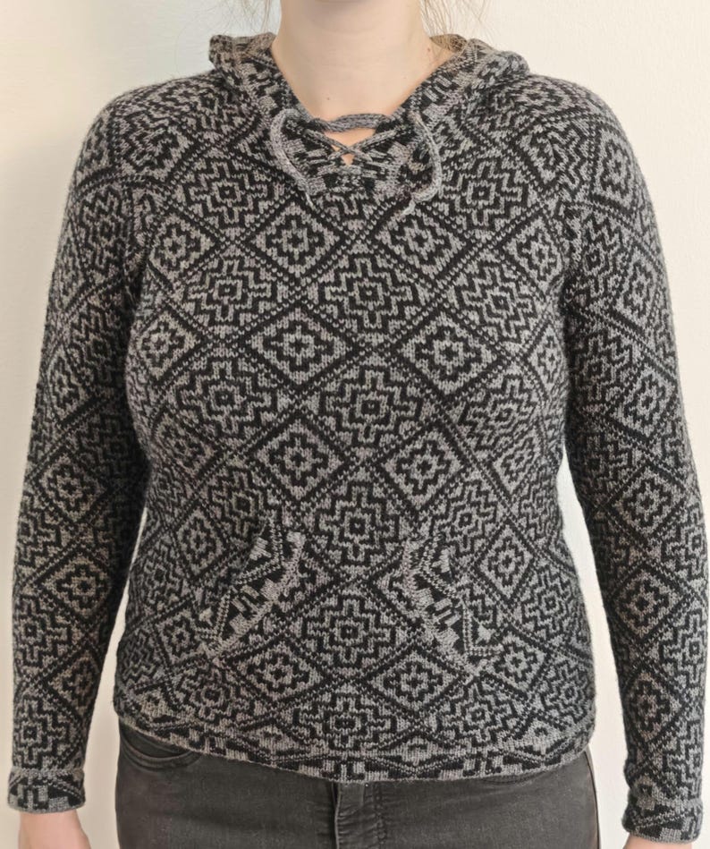 May include: A gray and black hooded sweater with a geometric pattern. The sweater features a drawstring neckline, long sleeves, and a front pocket. The pattern is a repeating diamond design.