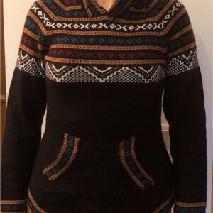 May include: Black hooded sweater with a patterned design in white, brown, and blue. The sweater has a kangaroo pocket and ribbed cuffs. The hood and pocket edges are trimmed with a contrasting pattern.