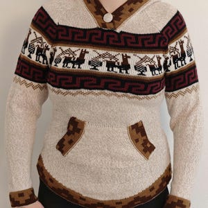 May include: Beige hooded sweater with geometric and llama patterns in brown, burgundy, and white. Features a button closure, kangaroo pocket, and ribbed cuffs. A cozy, warm knitwear garment.