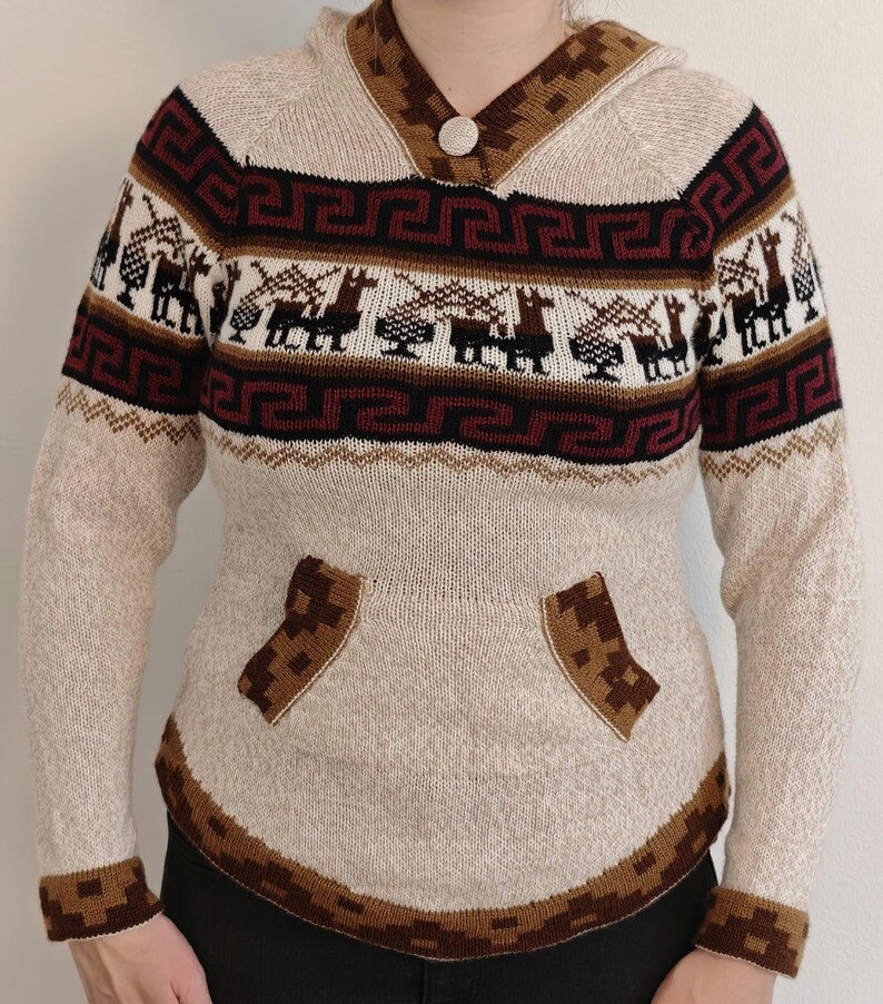 May include: Beige hooded sweater with geometric and llama patterns in brown, burgundy, and white. Features a button closure, kangaroo pocket, and ribbed cuffs. A cozy, warm knitwear garment.