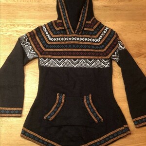 May include: Black hooded sweater with a geometric pattern in white, brown, and blue. The sweater has a kangaroo pocket and flared sleeves. The hood and hem are trimmed with a decorative border.