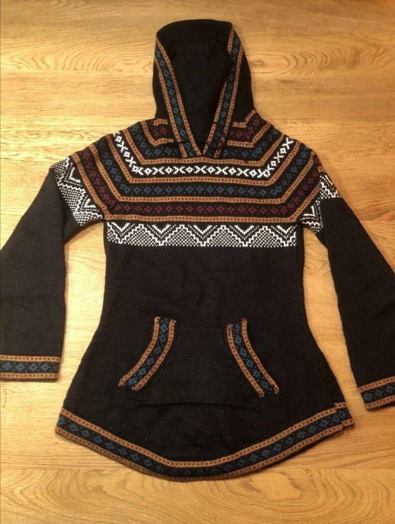May include: Black hooded sweater with a geometric pattern in white, brown, and blue. The sweater has a kangaroo pocket and flared sleeves. The hood and hem are trimmed with a decorative border.