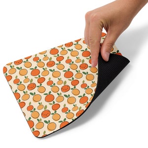May include: A mouse pad with a repeating pattern of orange fruit with leaves and a cartoon face. The mouse pad has a black rubber backing.