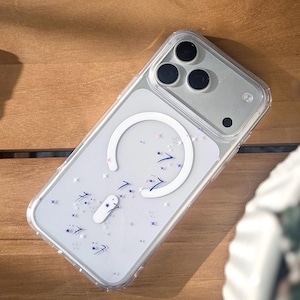 May include: Clear phone case with a white MagSafe ring and a design of blue arrows, stars, and a white shape. The case is on a wooden surface.