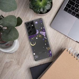 Peut inclure: Une coque de téléphone transparente avec un motif sur le thème de la galaxie. La coque présente un fond noir avec des étoiles, des planètes et une lune croissante de couleur violette, jaune et blanche. La coque porte également l'inscription "SAMSUNG".
