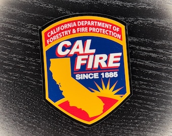 Op de afbeelding: Een schildvormige patch met de tekst "CAL FIRE" in witte letters over een gele omtrek van Californië. De patch bevat ook de tekst "CALIFORNIA DEPARTMENT OF FORESTRY & FIRE PROTECTION" en "SINCE 1885". De patch heeft een blauwe achtergrond met rode en gele accenten.
