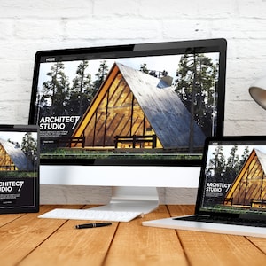 May include: A desktop computer, tablet, and laptop display a website for Architect Studio. The website features a modern A-frame cabin design set in a forest. A pen and keyboard sit on a wooden desk.