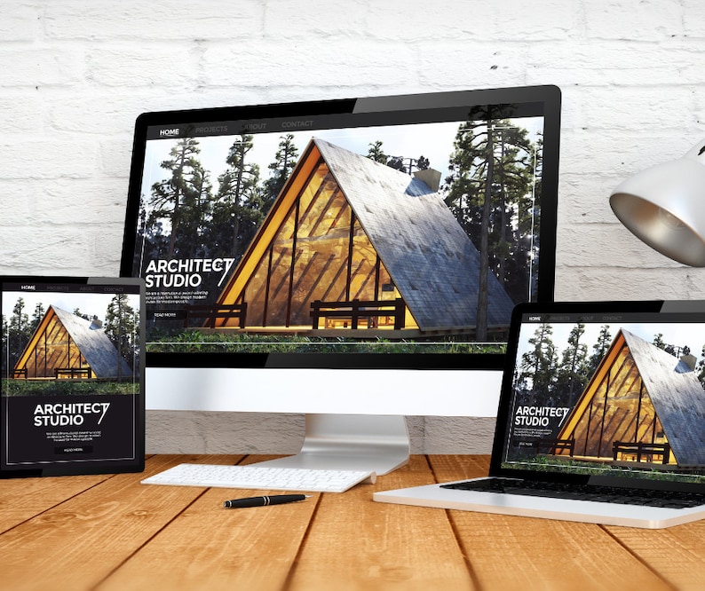 May include: A desktop computer, tablet, and laptop display a website for Architect Studio. The website features a modern A-frame cabin design set in a forest. A pen and keyboard sit on a wooden desk.